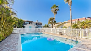 A swimming pool with a white fence, palm trees, and houses in the background. - Delightful condo with beach and pool access washer dryer (Belleair Beach)