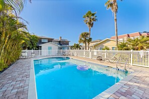A swimming pool with a white fence, palm trees, and houses in the background.