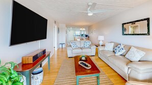 Ein Wohnzimmer mit Flachbildfernseher, Holztisch, beiges Sofa und Deckenventilator.