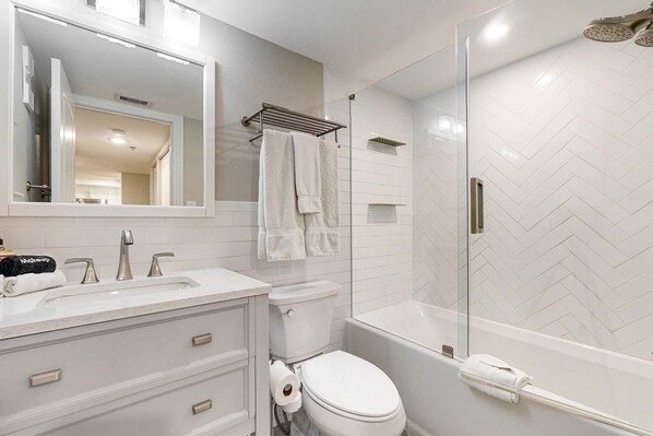 A modern bathroom with a white sink, two faucets, a toilet, and a glass-enclosed shower.
