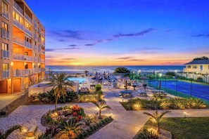 A hotel with a pool, outdoor seating, and a view of the ocean at sunset.