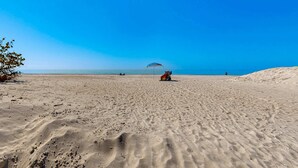 Une vaste plage de sable fin, parsemée d’empreintes, sous un ciel bleu et dégagé.