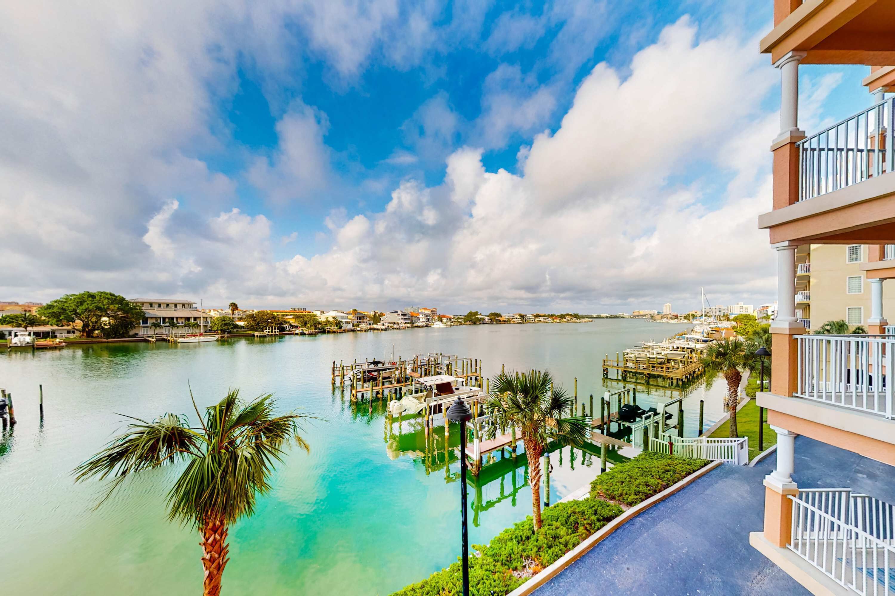 Vista al agua con muelle, palmeras y un edificio con balcones.