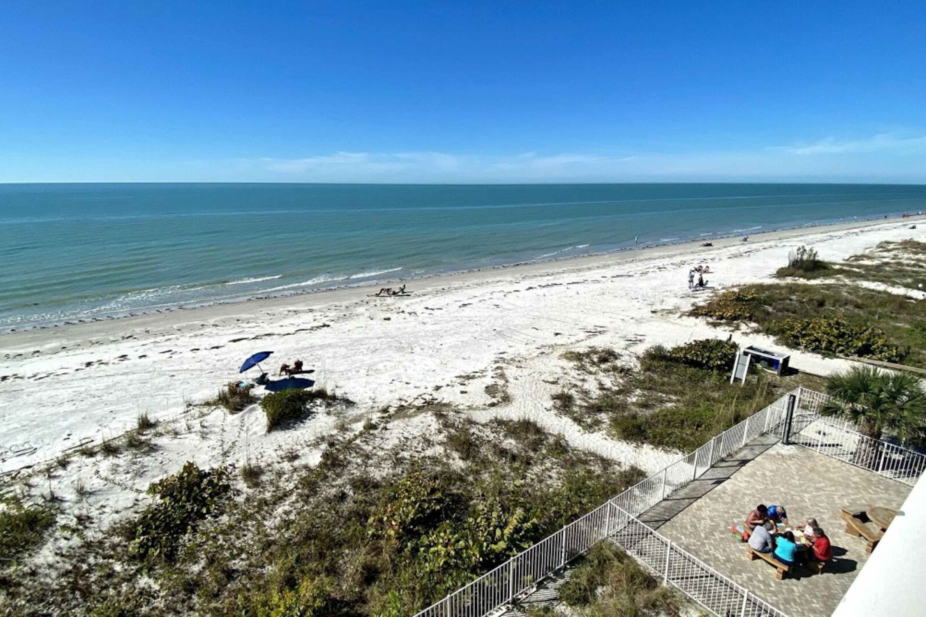 A beach view with a fenced patio area, some beachgoers, and a clear sky.
