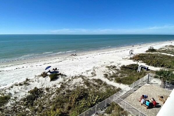 A beach view with a fenced patio area, some beachgoers, and a clear sky.