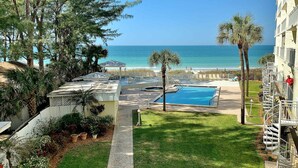 Zona de piscina con vista al océano, rodeada de árboles y un edificio con balcón.
