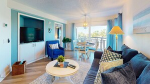 Ein Wohnzimmer mit Fernseher, blauem Sessel und einem Essbereich mit Tisch und Stühlen.