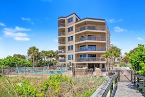 Um hotel com vários andares, varandas, piscina e um calçadão de madeira.