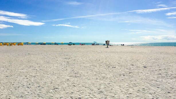 Une vaste plage de sable, parsemée de parasols et dotée d’une tour de surveillance pour les sauveteurs.