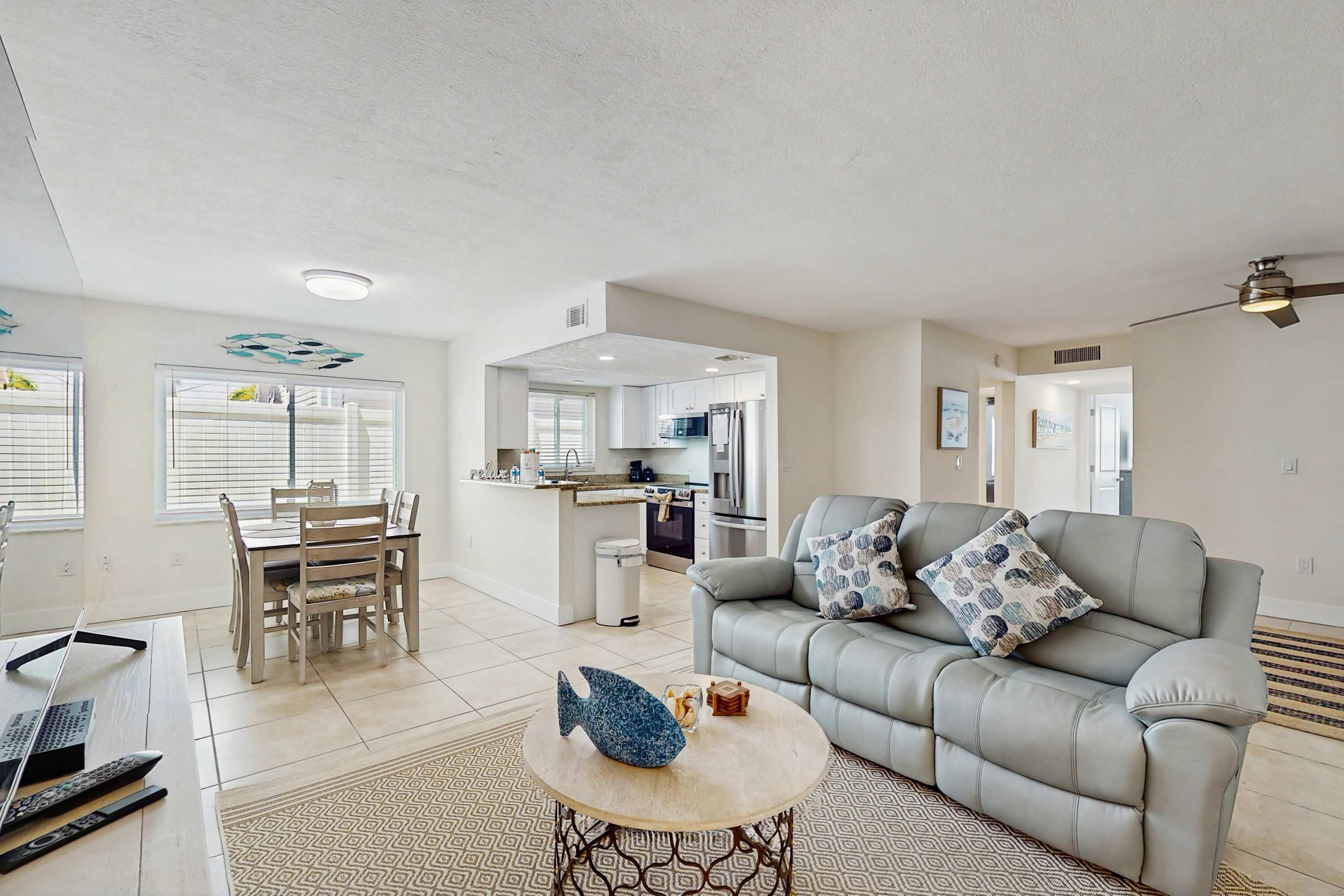 A spacious living area with a grey sofa, a dining table, and a kitchen in the background.