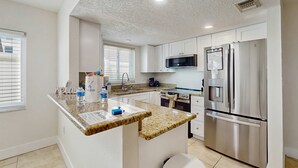 Une cuisine moderne dotée de plans de travail en granit, d’appareils électroménagers en acier inoxydable et de meubles blancs.