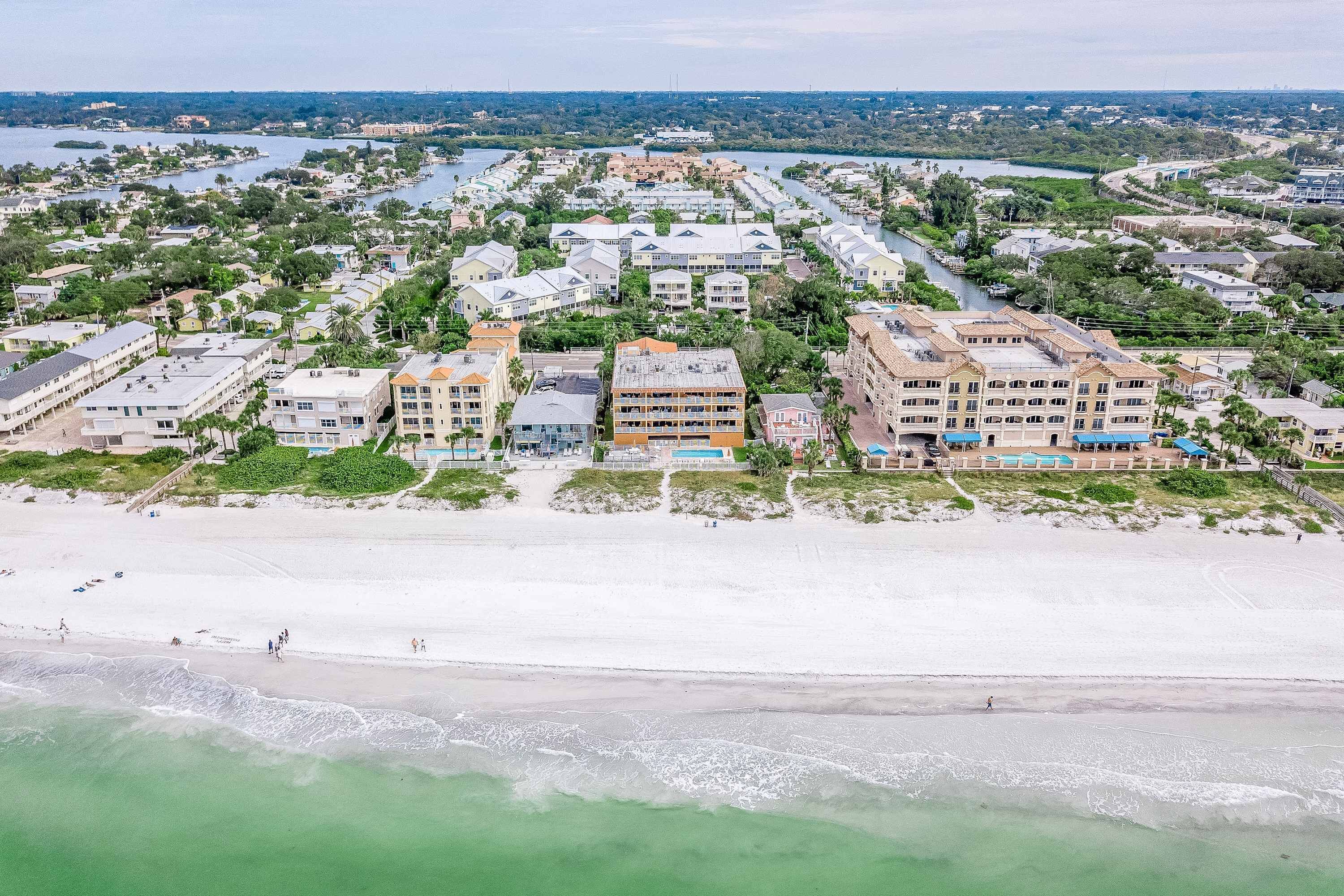 Vista aerea di una zona residenziale costiera con proprietà fronte spiaggia, tra cui edifici a più piani e una spiaggia sabbiosa.