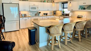 Een moderne keuken met witte kastjes, een groot eiland met barkrukken, een koelkast, magnetron en koffiezetapparaat.