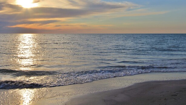 Una playa con el sol reflejado en el agua, creando un ambiente tranquilo y sereno.