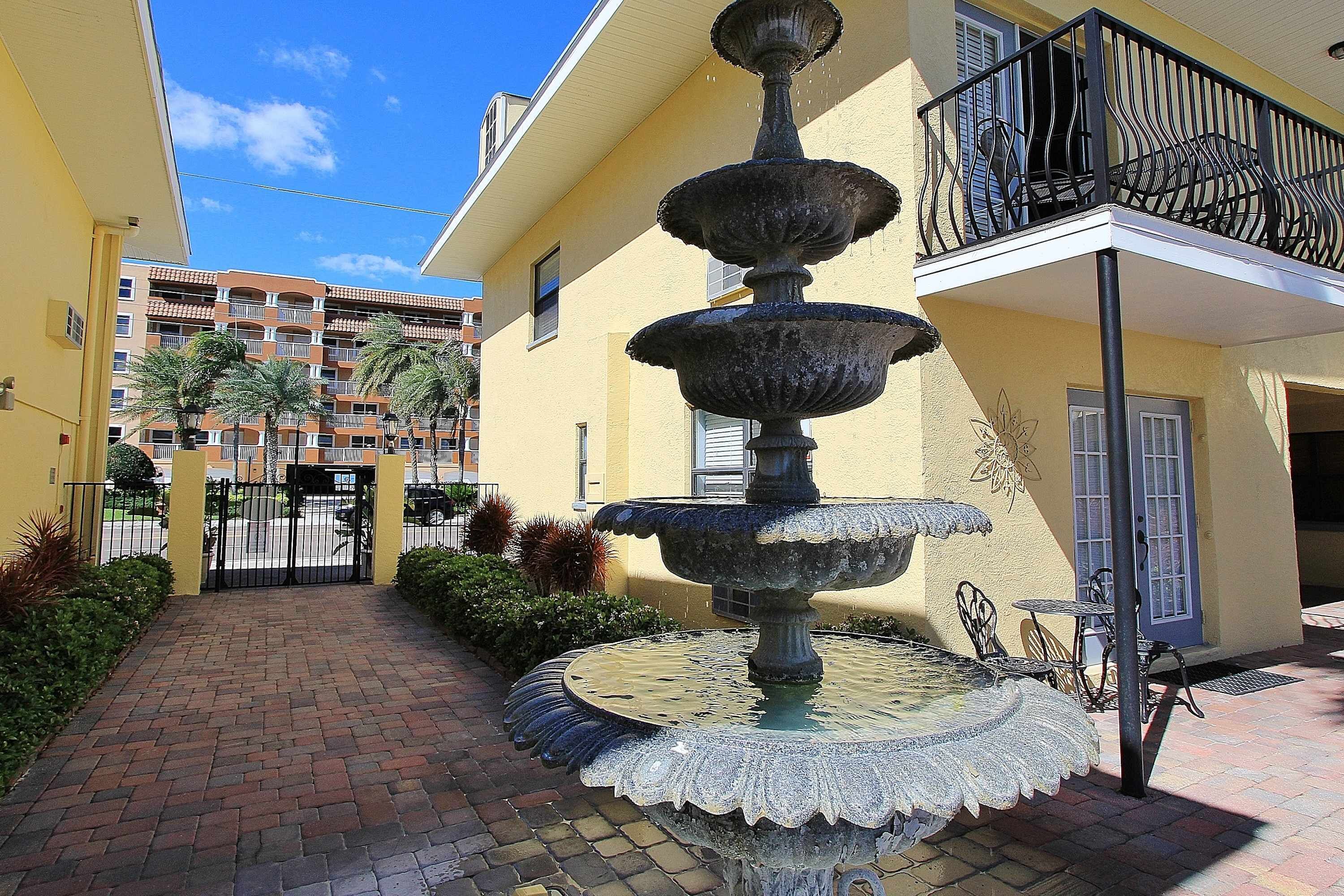 Un patio con una fuente escalonada, una entrada protegida por una reja y un edificio con balcones.