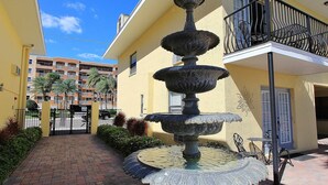 Un patio con una fuente escalonada, una entrada protegida por una reja y un edificio con balcones.