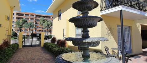 Un patio con una fuente escalonada, una entrada protegida por una reja y un edificio con balcones.
