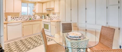 A modern kitchen with white cabinets, a glass dining table, wicker chairs, and a ceiling fan.