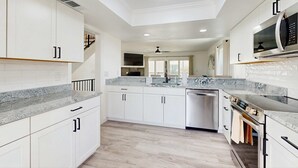 Una cocina moderna con armarios blancos, encimeras de granito y electrodomésticos de acero inoxidable.