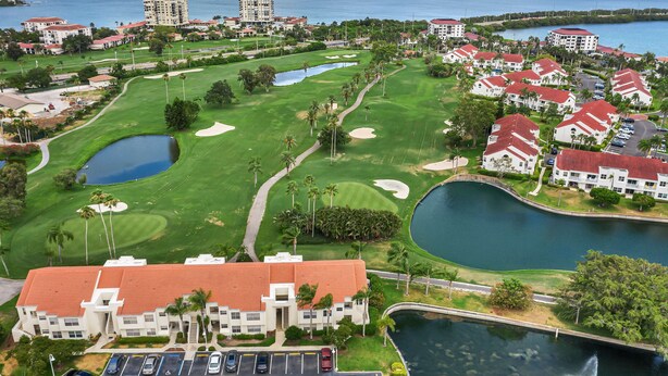 A golf course with a large pond, surrounded by buildings with red roofs and white walls. - Beautiful condo near beaches and activities with pool access and golf course view (St. Petersburg)