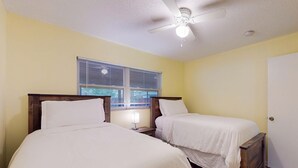 Een slaapkamer met twee bedden, een plafondventilator, een raam met zonwering en een deur.
