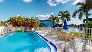 A swimming pool with a blue border, surrounded by palm trees and a white fence. - Family-Friendly, Canal Front Condo Near Beach | Close to Island Events (Treasure Island)