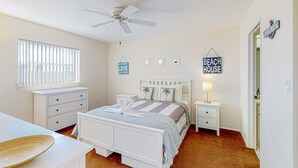 A bedroom with a bed, bedside tables, a ceiling fan, a window with blinds, and a sign that reads "BEACH HOUSE". - Family-Friendly, Canal Front Condo Near Beach | Close to Island Events (Treasure Island)