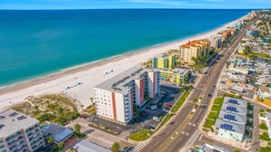 Vista aérea de una zona hotelera frente al mar, con acceso directo a la playa, varios edificios y una carretera que conduce hasta la arena.
