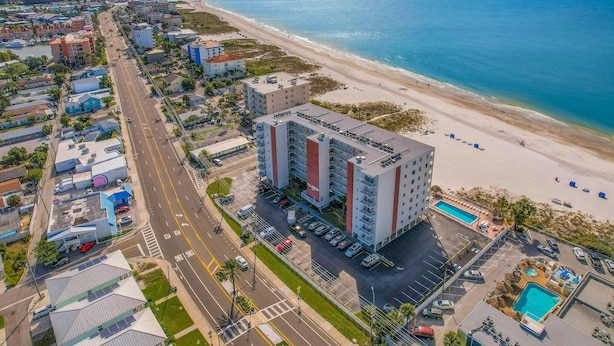 Vue aérienne d’un hôtel situé sur la côte, composé de plusieurs bâtiments, d’un parking et d’une plage.
