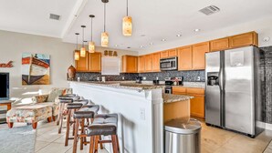 Una cocina moderna con armarios de madera, un refrigerador de acero inoxidable y una zona de bar con taburetes.