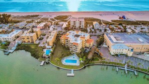 Vista aérea de un complejo turístico costero con varias construcciones, una piscina y un puerto deportivo.