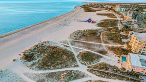 Vista aérea de una playa con un paseo marítimo, edificios y una zona de piscina.
