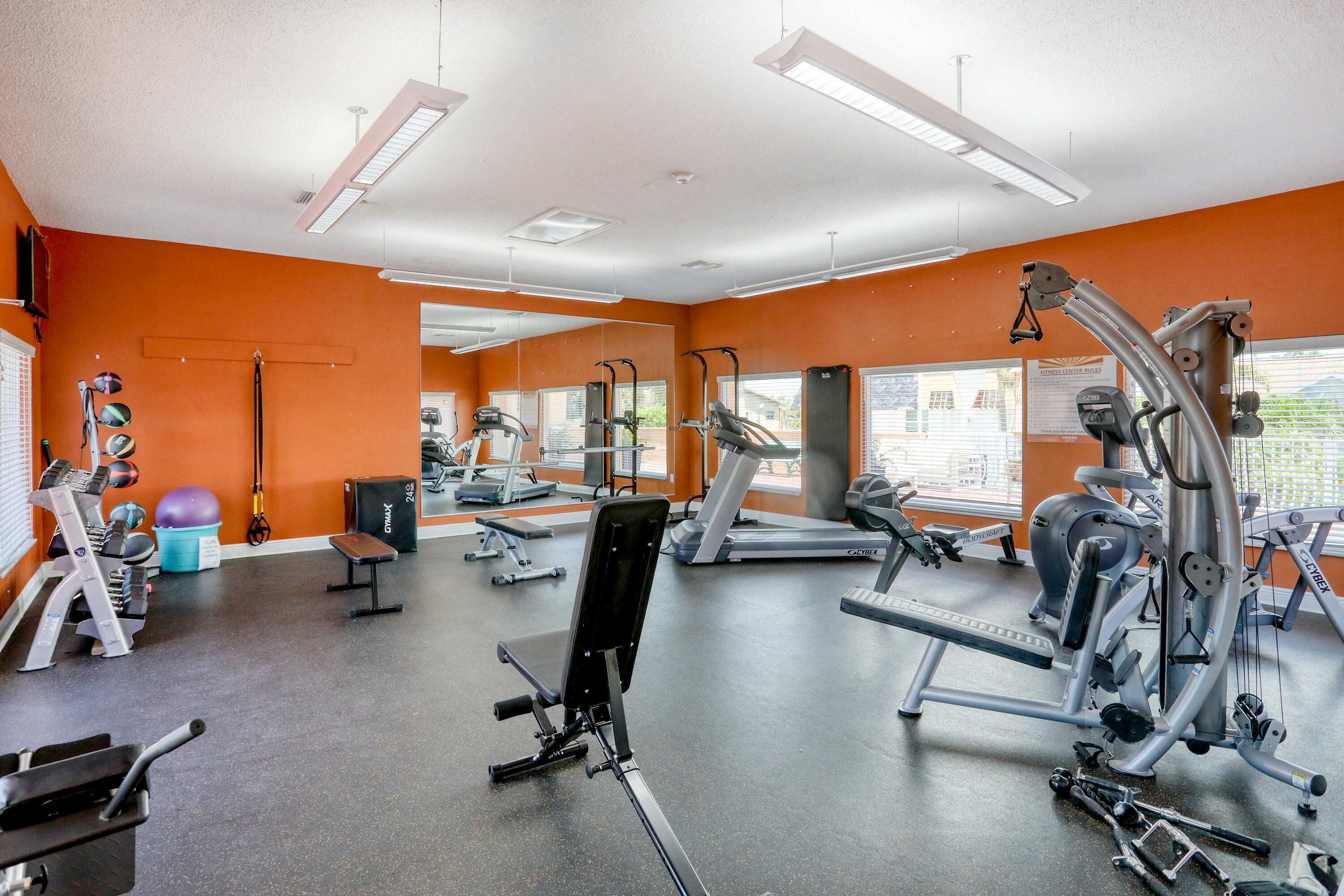 A gym with various exercise equipment, large windows, and orange walls.