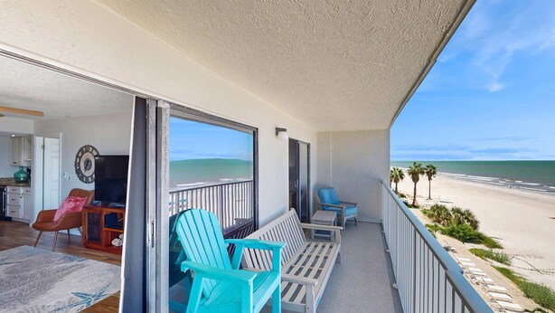 Ein Balkon mit Blick auf den Strand, eine Sitzecke mit Stühlen und Tisch sowie ein Zimmer mit Fernseher und einer Uhr.
