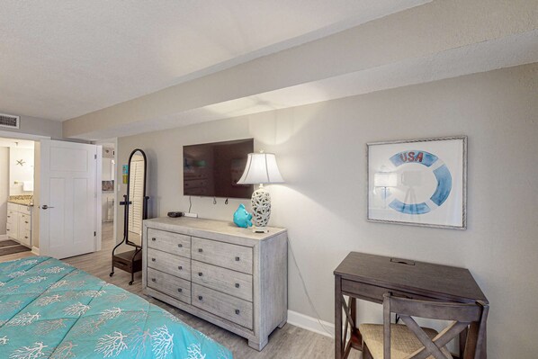 A bedroom with a bed, dresser, vanity, mirror, lamp, and a wall with a framed picture. - Renovated beachfront condo with heated pool amazing Gulf views and washer dryer (Madeira Beach)