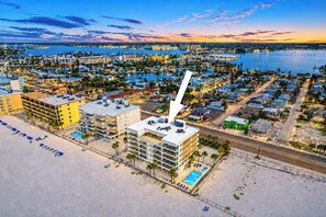 An aerial view of a coastal city with a prominent hotel featuring a rooftop pool and a large white spire. - Renovated beachfront condo with heated pool amazing Gulf views and washer dryer (Madeira Beach)