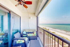 Ein Balkon mit Korbmöbeln, einem Deckenventilator und Blick auf den Strand.