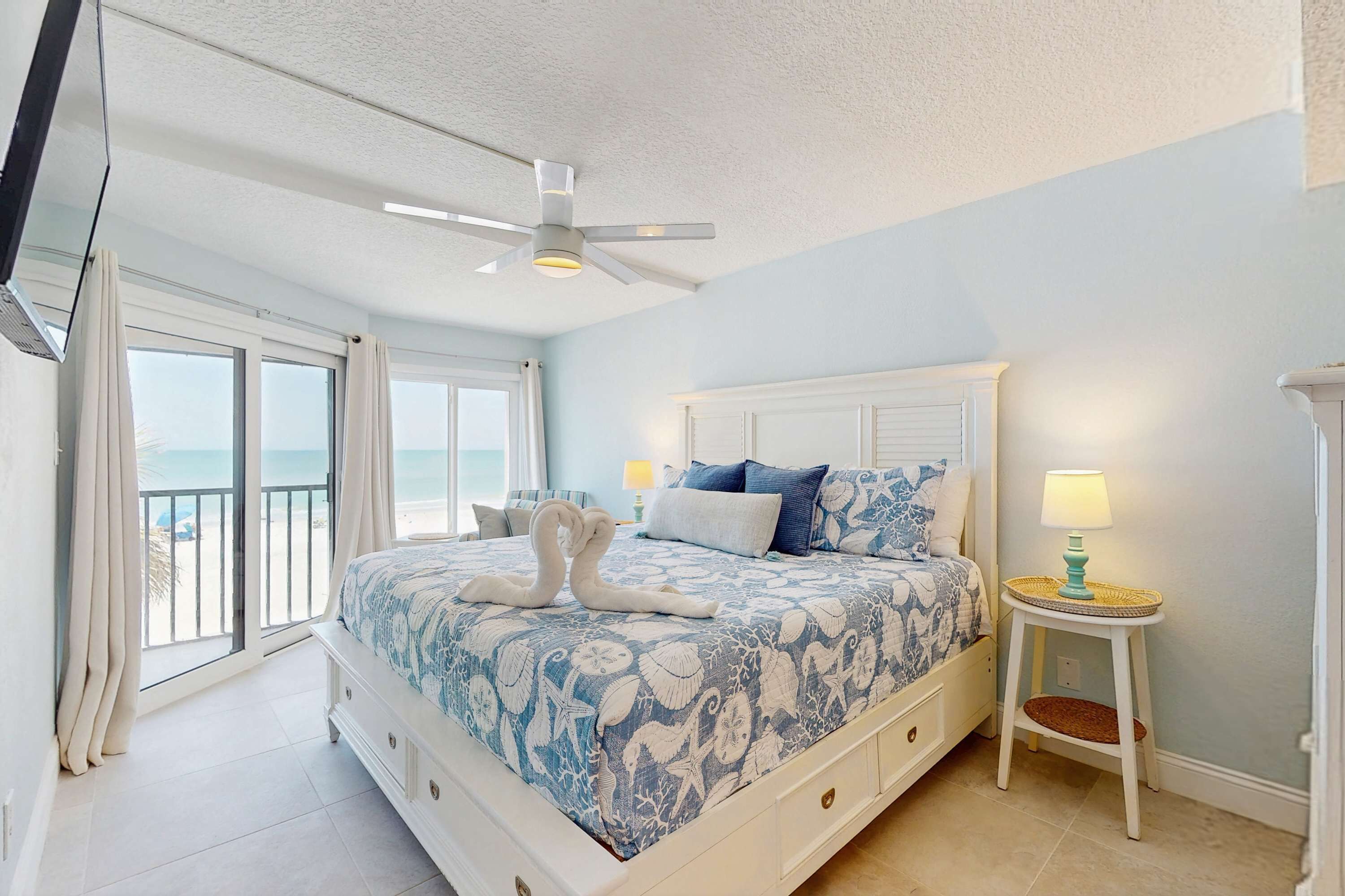 Ein Schlafzimmer mit Bett, Deckenventilator, Nachttisch und Blick auf den Strand.