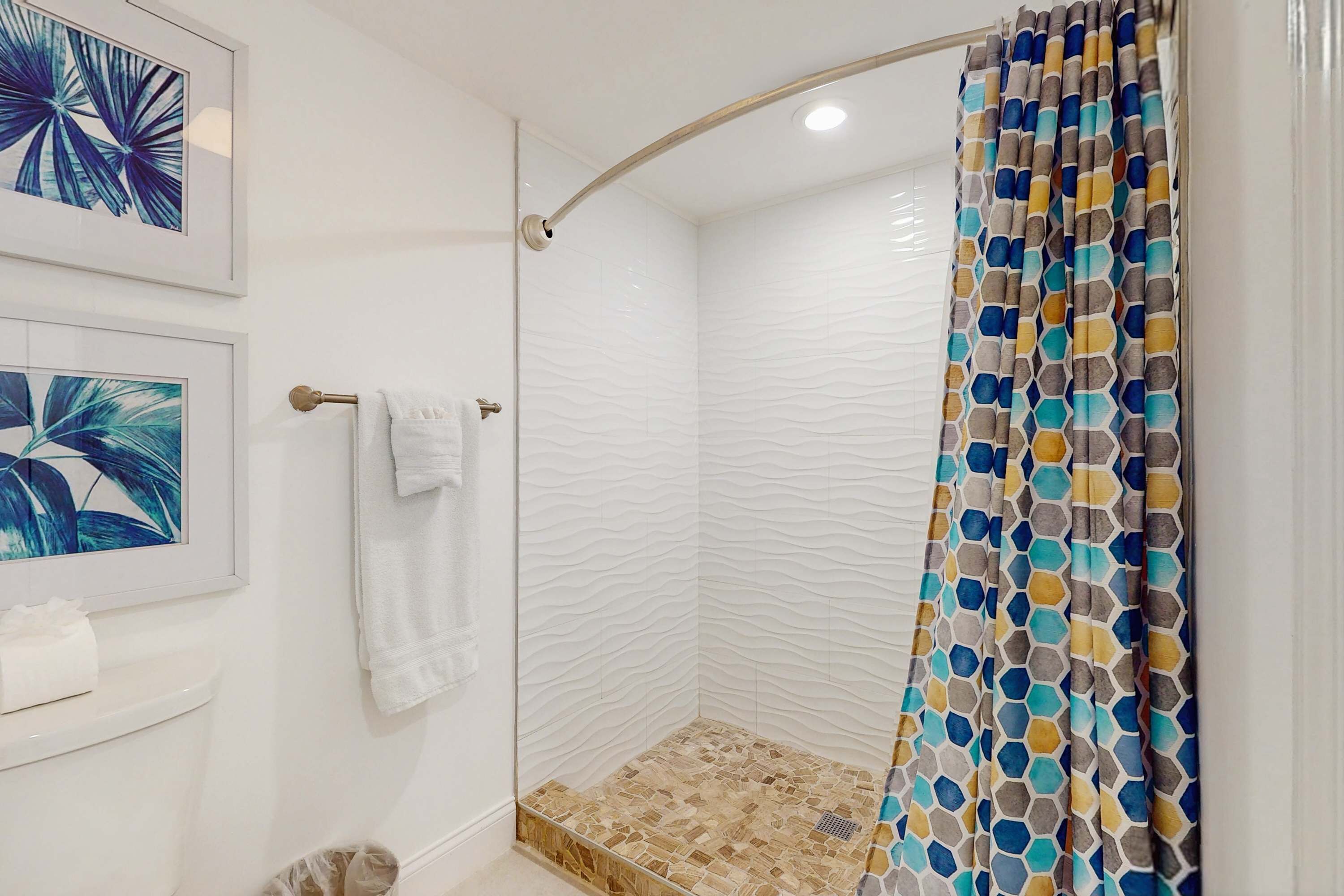 Un baño moderno con cabina de ducha de vidrio, paredes blancas con textura y cortina de ducha estampada.