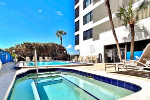 A swimming pool with clear blue water, surrounded by lounge chairs and palm trees. - Beautiful oceanfront condo in Madeira Beach w balcony and pool (Madeira Beach)