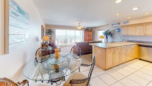 Une cuisine spacieuse avec une table à manger en verre, des meubles de rangement en bois et une vue sur l’extérieur.