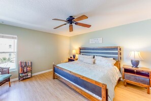 A bedroom with a bed, a ceiling fan, a bookshelf, two bedside tables with lamps, and a window with blinds.