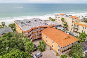 A beachfront hotel with multiple balconies, a parking area, and a view of the beach and ocean.