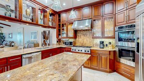 Eine großzügige Küche mit Granit-Arbeitsplatten, Edelstahlgeräten, Holzschränken und Pendelleuchten.