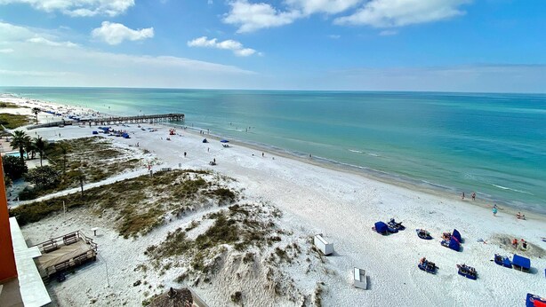 A beach with a pier extending into the water, sandy beach, and several beach umbrellas. - Beachfront condo with Gulf view balcony and central AC snowbirds OK (Indian Shores)