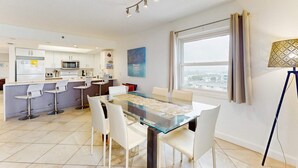 A modern kitchen with white cabinets, a microwave, and a dining area with a glass table and white chairs. - Beachfront condo with Gulf view balcony and central AC snowbirds OK (Indian Shores)