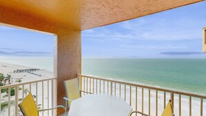 A balcony with a table and chairs, overlooking a beach and ocean. - Beachfront condo with Gulf view balcony and central AC snowbirds OK (Indian Shores)