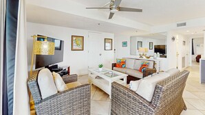 A spacious living room with wicker furniture, a ceiling fan, a flat-screen TV, and a large mirror reflecting the room. - Beachfront condo with Gulf view balcony and central AC snowbirds OK (Indian Shores)