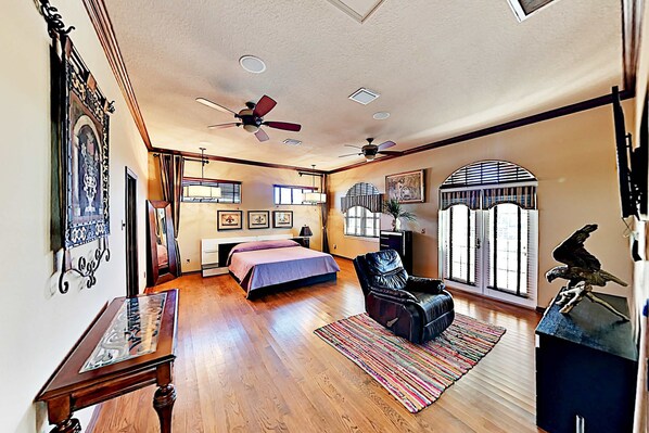 A spacious bedroom with a large bed, a leather chair, a desk, and a ceiling fan.