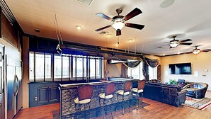 A spacious living area with a bar, multiple ceiling fans, and a large TV.
